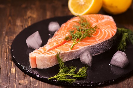 Raw salmon steak with lemon and herbs over wooden background. Healthy food conceptの写真素材