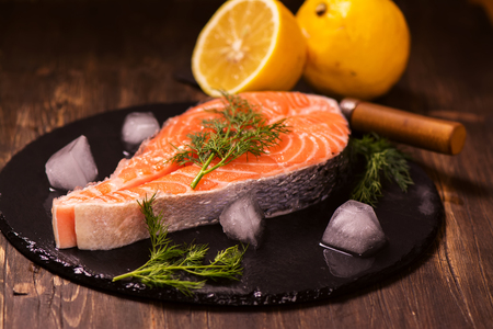 Raw salmon steak with lemon and herbs over wooden background. Healthy food conceptの写真素材