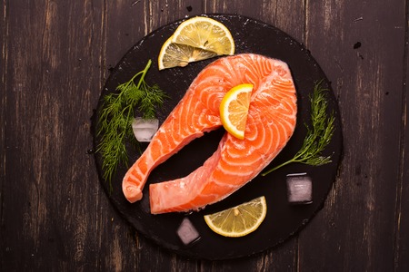 Raw salmon steak with lemon and herbs over wooden background. Healthy food conceptの写真素材