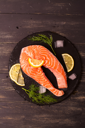 Raw salmon steak with lemon and herbs over wooden background. Healthy food conceptの写真素材