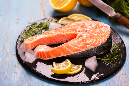 Raw salmon steak with lemon and herbs over wooden background. Healthy food conceptの写真素材