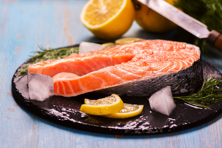 Raw salmon steak with lemon and herbs over wooden background. Healthy food conceptの写真素材