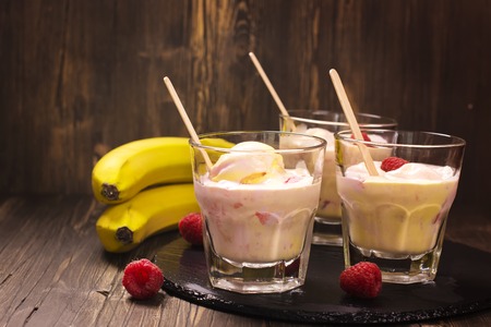 Refreshing milk cocktail with ice cream scoops, raspberry and banana over vintage table. Selective focusの写真素材