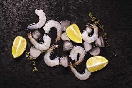 Raw prawns with lime and thyme over black wet stone background. Top viewの写真素材