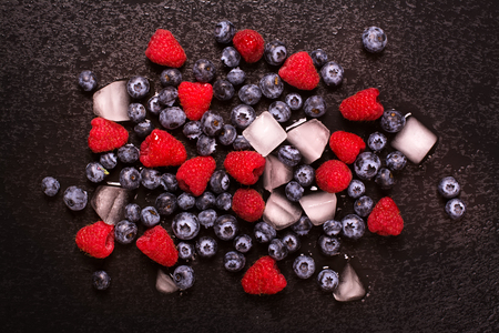 Ripe blueberry and raspberry with ice cubes over black wet stone background. Toned image. Selective focusの写真素材