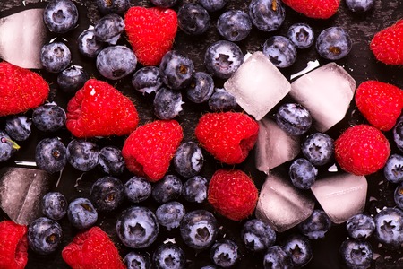Ripe blueberry and raspberry with ice cubes over black wet stone background. Toned image. Selective focusの写真素材