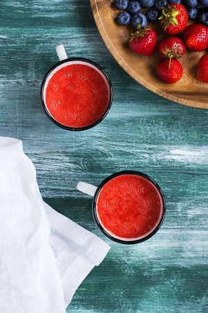 Strawberry soup in retro enamel mugs over wooden tableの写真素材