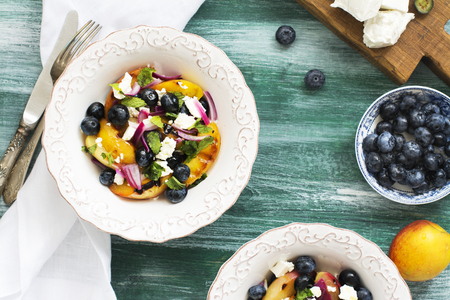 Delicious summer salad with grilled peaches, blueberry and feta cheese in white bowl over wooden background. Selective focusの写真素材