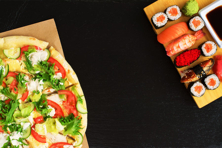 Sushi vs pizza. Business lunch concept, black stone background. Space for textの写真素材