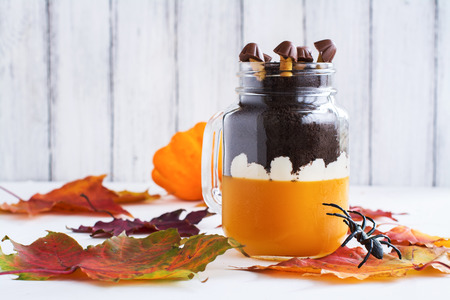 Layered halloween dessert with pumpkin jello, cream and chocolate cookies in glass jars on autumn background. Selective foucsの写真素材