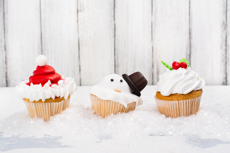 Funny christmas cupcakes on white background. Delicious gift for xmas or new year. Melting snowman, santas hat and omela decorated cakes. Space for text. Selective focusの写真素材