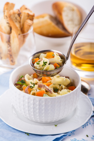 Homemade chicken noodle soup with vegetables. Selective focus on soup in ladle.の写真素材