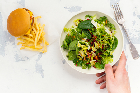 Young man making choice between healthy salad and fast food.の写真素材