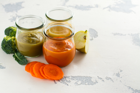 Assortment of baby food in glass jars. Homemade vegetable and fruit puree with ingredients on white background. Space for textの写真素材