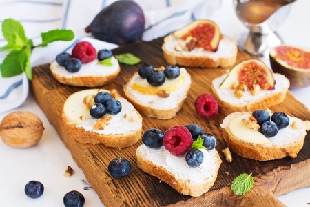 Small bruschetta with fruits, berries, honey and walnuts on wooden board. Selective focusの写真素材