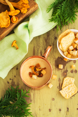 Chanterelle cream soup in coper mug served with croutons and crackers over rustic wooden background. Vintage style. Selective focusの写真素材