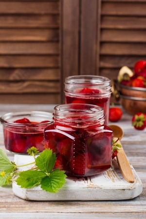 Homemade strawberry jam with whole berries in glass jars on wooden table. Toned image. Copy spaceの写真素材