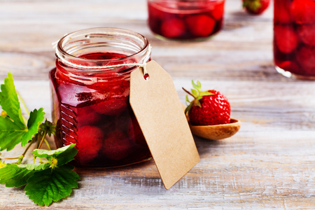 Homemade strawberry jam with whole berries in glass jars on wooden table. Toned image. Copy spaceの写真素材