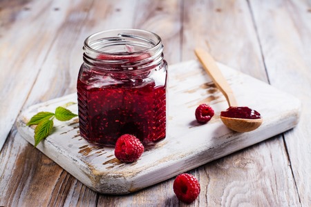 Raspberry jam in a glass jar, fresh raspberry and croissant on wooden table. Space for text