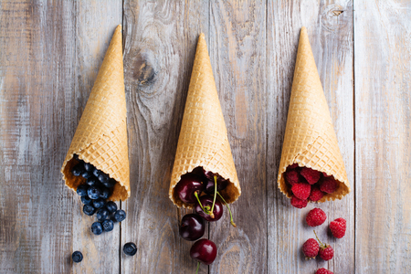 Sweet summer berries in waffle cones on wooden background. Space for textの写真素材