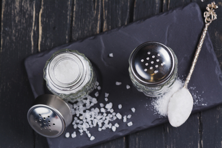 Glass salt shakers with sea salt coarse and fine on dark wooden tableの写真素材