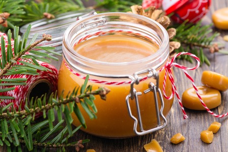 Homemade salted caramel sauce in a glass jar and Christmas decor on wooden backgroundの写真素材