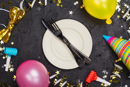Bright festive carnival table setting with plate and cutlery on black stone table decorated with party accessoriesの写真素材