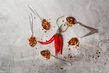 Bunch of red hot chilli peppers and flakes in spoons on grey stone kitchen table