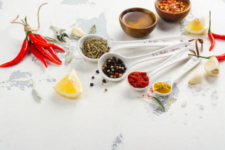 Dry herbs and spices in measuring spoons on white stone kitchen tableの写真素材