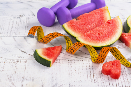 Fresh ripe watermelon slices, dumbbells and measuring tape on wooden backgroundの写真素材