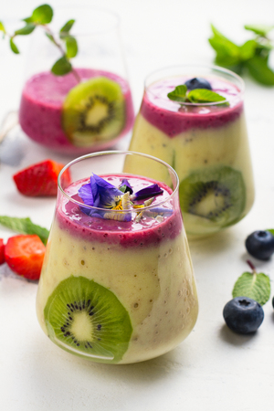 Colorful detox layered smoothie with natural edible flowers, berries and mint on white background. Copy spaceの写真素材