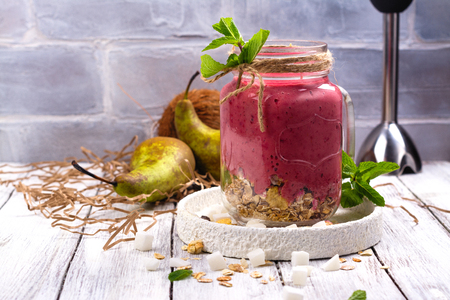 Colorful detox summer smoothie with red berries, pear, granola and dry coconut cubes on light background. Copy spaceの写真素材