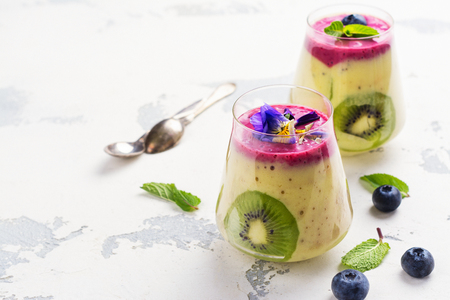 Colorful detox layered smoothie with natural edible flowers, berries and mint on white background. Copy spaceの写真素材