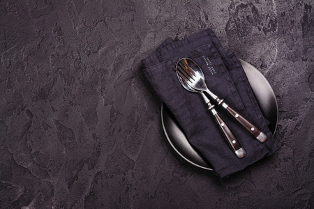 Empty black plate and silverware on dark stone backgroun. Top view. Copy spaceの写真素材