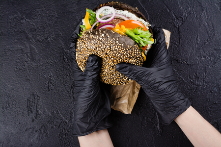 Womans hands in black rubber gloves are holding juicy black bun burgerの写真素材