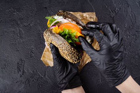 Womans hands in black rubber gloves are holding juicy black bun burgerの写真素材