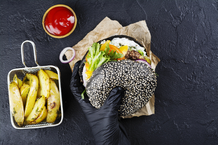 Womans hands in black rubber gloves are holding juicy black bun burgerの写真素材