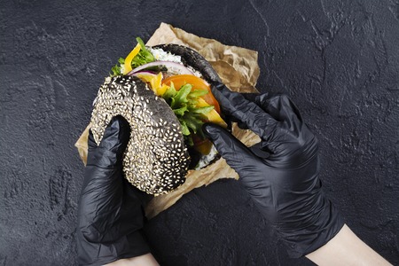Womans hands in black rubber gloves are holding juicy black bun burgerの写真素材