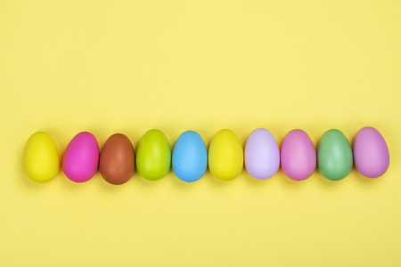 Row of bright colorful easter eggs on sunny yellow backgroundの写真素材