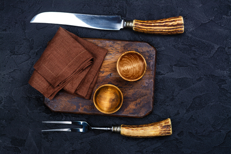 Wooden cutting board, bowl for spices and vintage fork and knife on stone black backgroundの写真素材