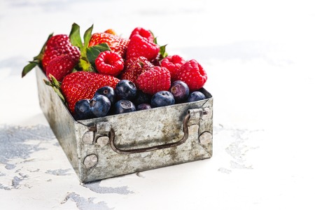 Fresh mix of berries in a metal box on white stone backgroundの写真素材