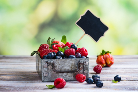 Fresh mix of berries in a metal box on white stone backgroundの写真素材