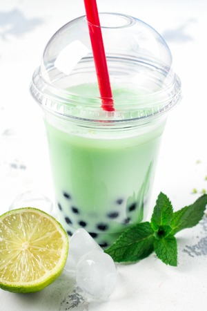 Refreshing homemade iced milky bubble tea with tapioca pearls. Lime and mint bubble tea in plastic cup on white background. Copy spaceの写真素材