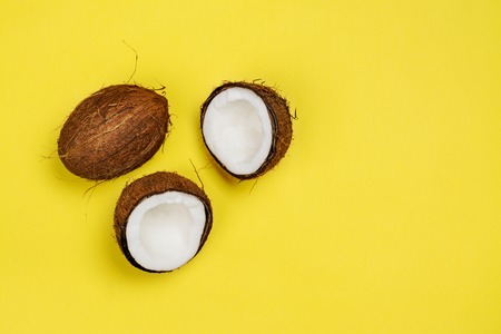 Coconut halves and leaves on yellow backgroundの写真素材