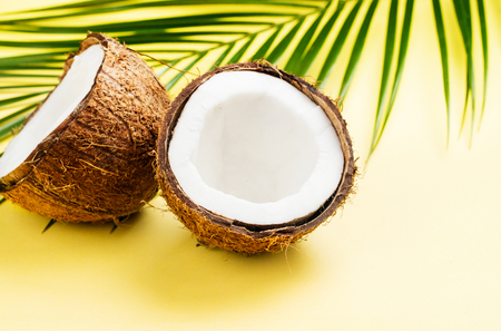 Coconut halves and leaves on yellow backgroundの写真素材