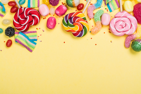 Candies, lollipops and jelly worms on yellow backgroundの写真素材