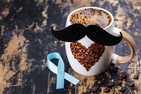 Men's health awareness concept - month of growing moustache. Coffee, paper moustache and blue ribbon on wooden table. Copy spaceの写真素材