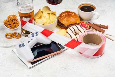 Dopamine fasting background. Life without social media, gadget and food detox concept. Red and white signal ribbon covering junk food and digital devices. Copy spaceの写真素材