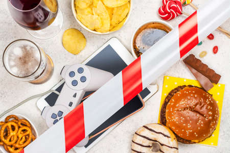 Dopamine fasting background. Life without social media, gadget and food detox concept. Red and white signal ribbon covering junk food and digital devices. Copy spaceの写真素材