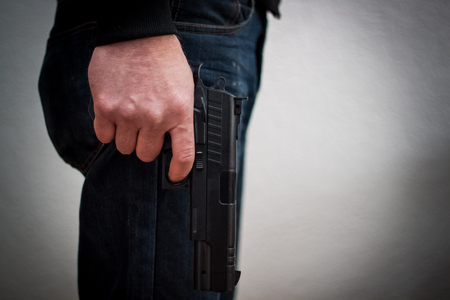 Killer holding a gun to his feet, white background in front of him, robbery, murder, crime